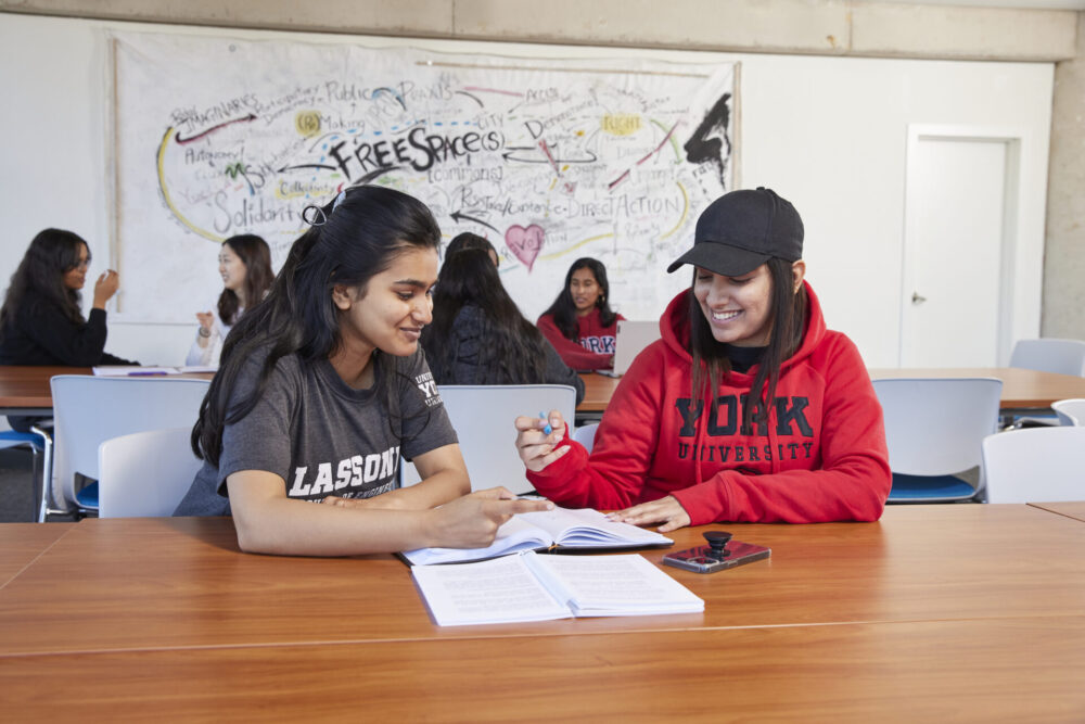 Two women smiling and looking down at a notebook