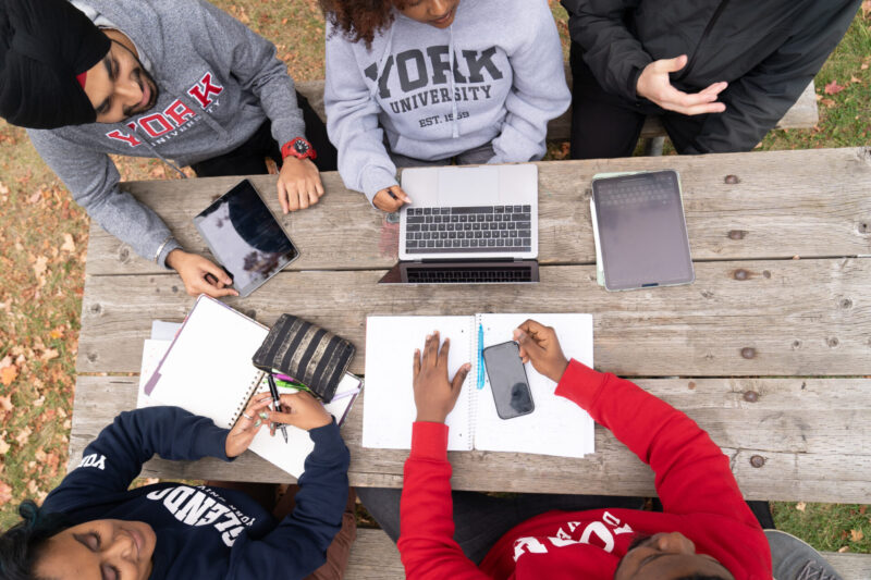 Students sitting around a picnic table with laptop and notebooks.