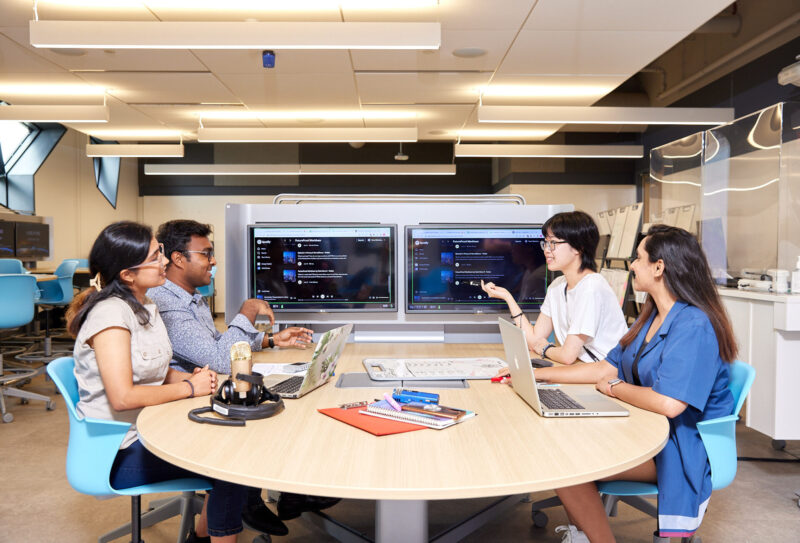 Individuals sitting around a table with laptops and a microphone