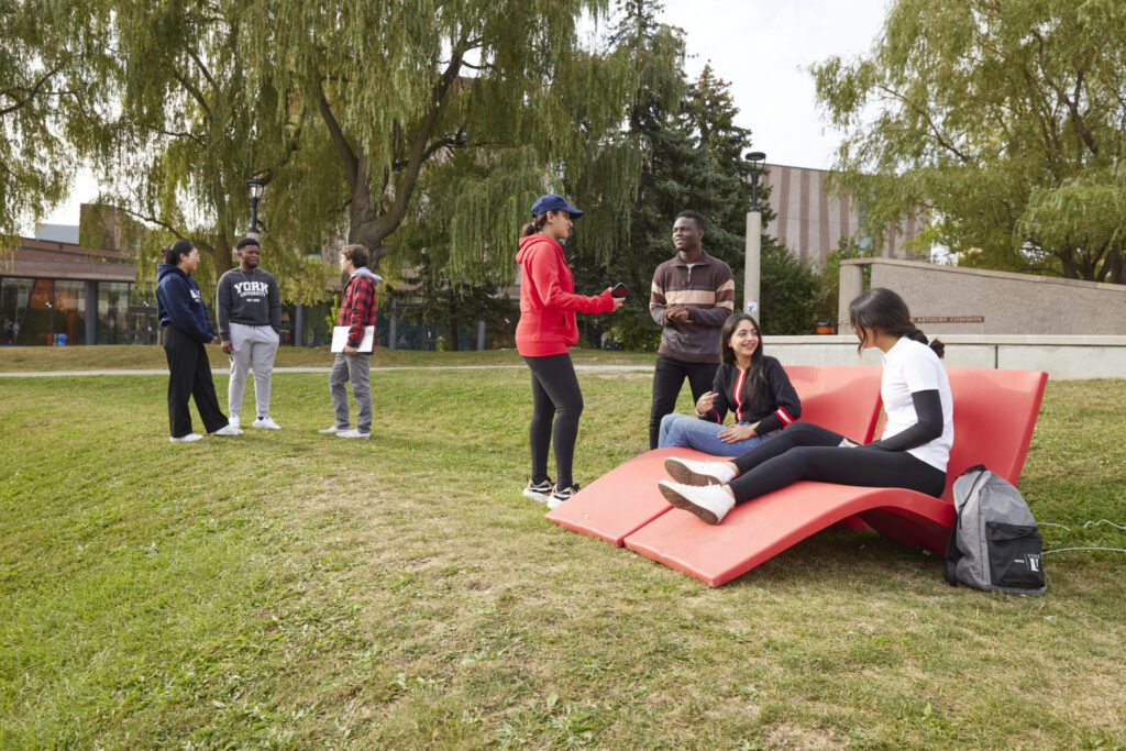 Students sitting in red lawn chairs on grass