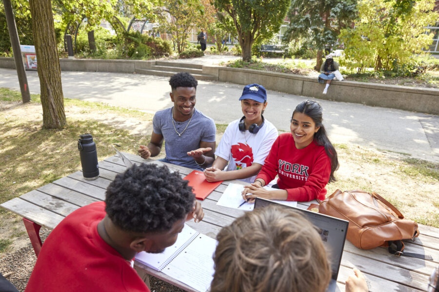 Students sitting at a picnic table with notebooks and laptop