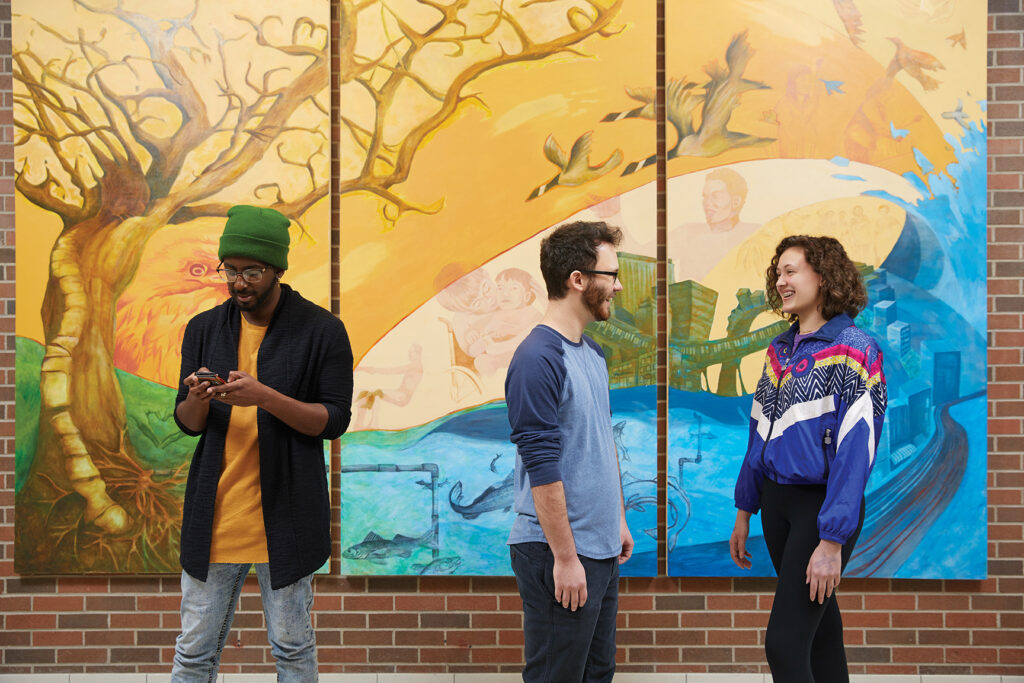 Students standing in front of a mural on the wall