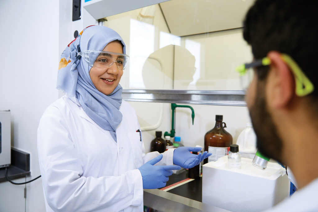 Two people wearing safety goggles and lab coats in a lab