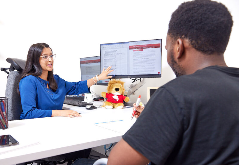 Two individuals sitting across from one another while one person is pointing at the computer