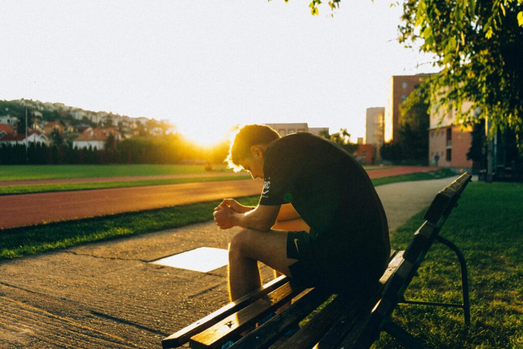 man sitting on bench near track field while sun is setting