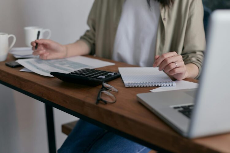 Person working at the desk with notebook, laptop, calculator and cups