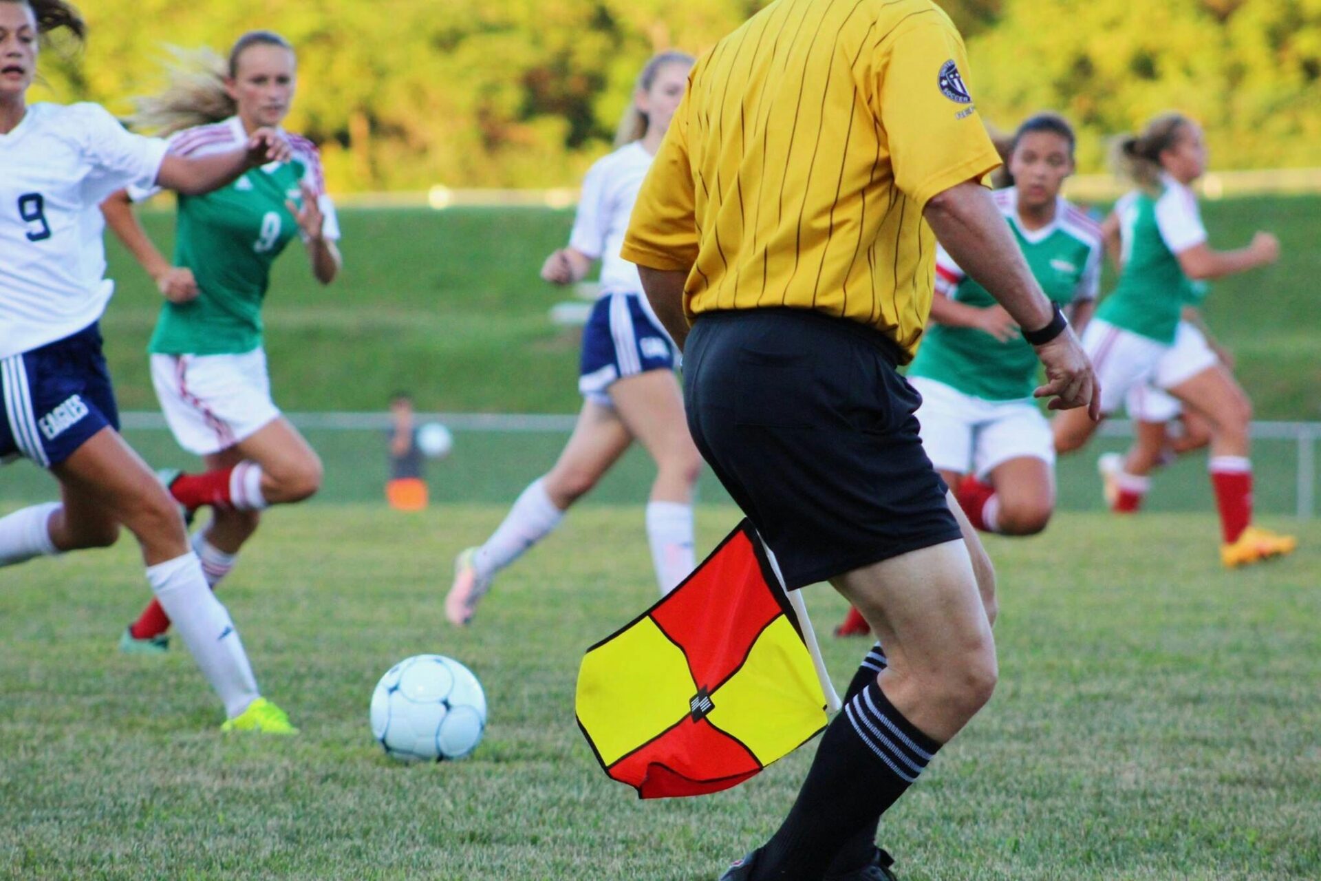 Athletes playing soccer outdoors with referee watching