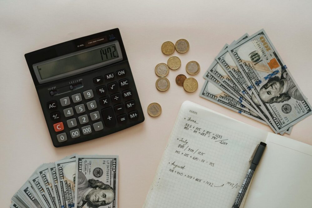 Photo of calculator, money bills, coins, notebook and pen