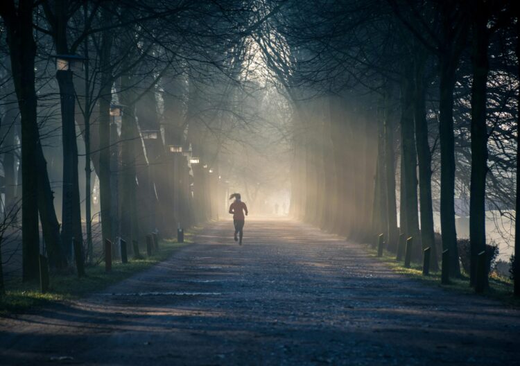 Person running near street between tall trees