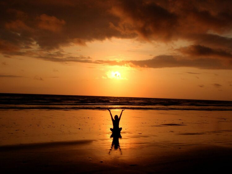 Silhouette of person raising hands on the beach