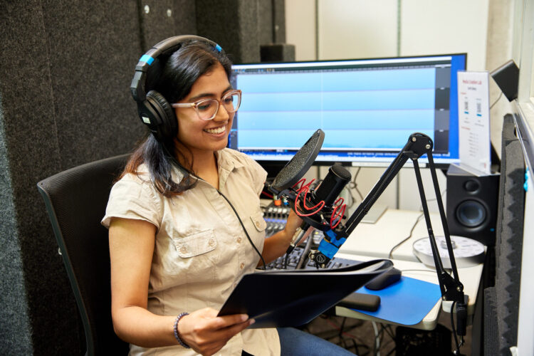 Woman wearing headphones and sitting by a microphone and audio equipment