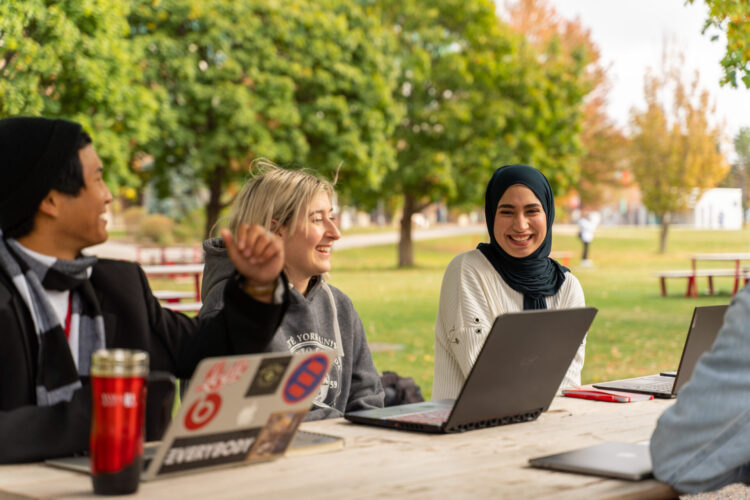 Students sitting at the picnic table with laptops