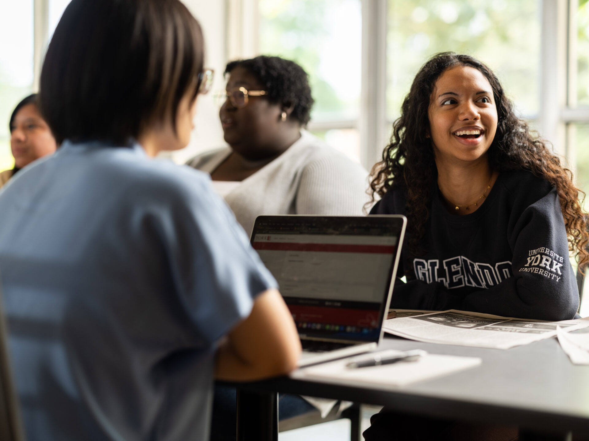 Two students sitting across each other with a laptop on the table