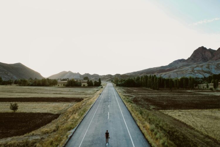 Person standing alone on a country road with mountains