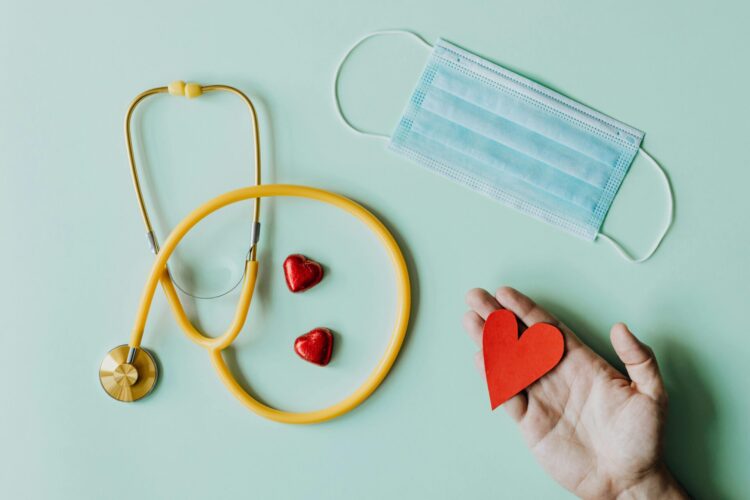 Medical stethoscope, mask and person's hand holding a red paper heart