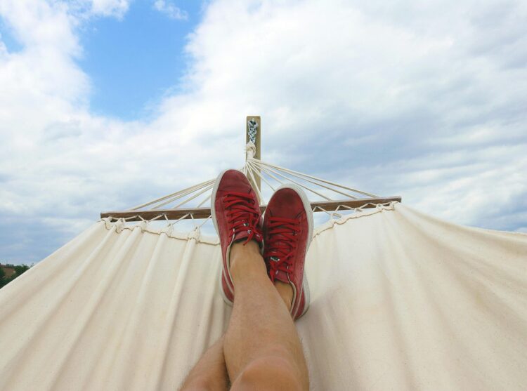 Person wearing pair of red and white sneakers and resting their feet on a hammock