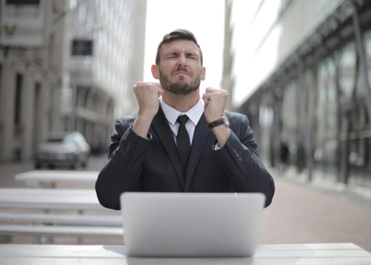 Upset man in black suit sitting on a chair by buildings