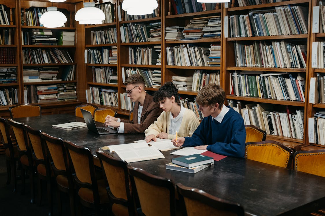 Three people studying in the library with bookshelves behind