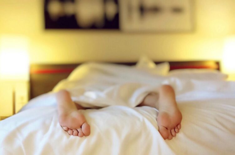 Feet of person lying on bed under white blanket