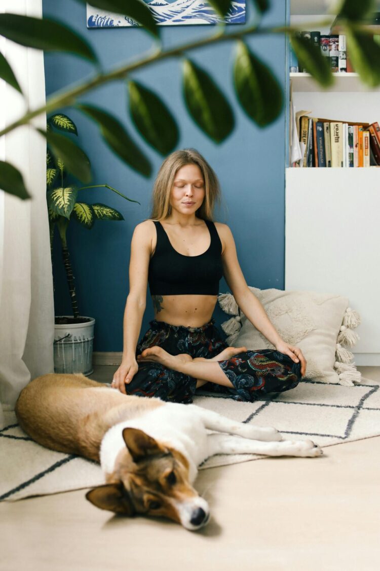 Woman sitting on the floor and meditating with a dog lying next to her