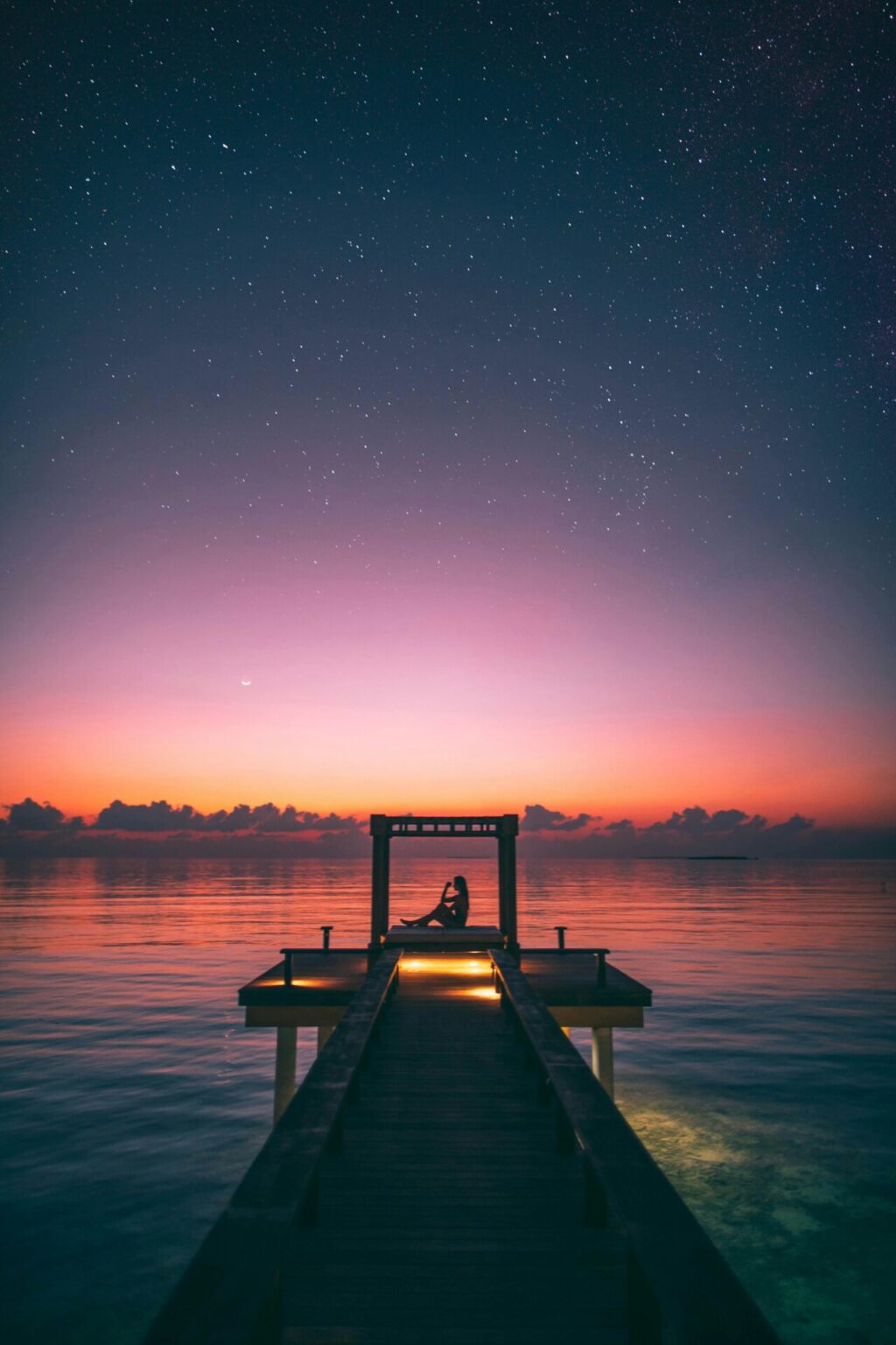 Silhouette of person sitting on boardwalk at sunset