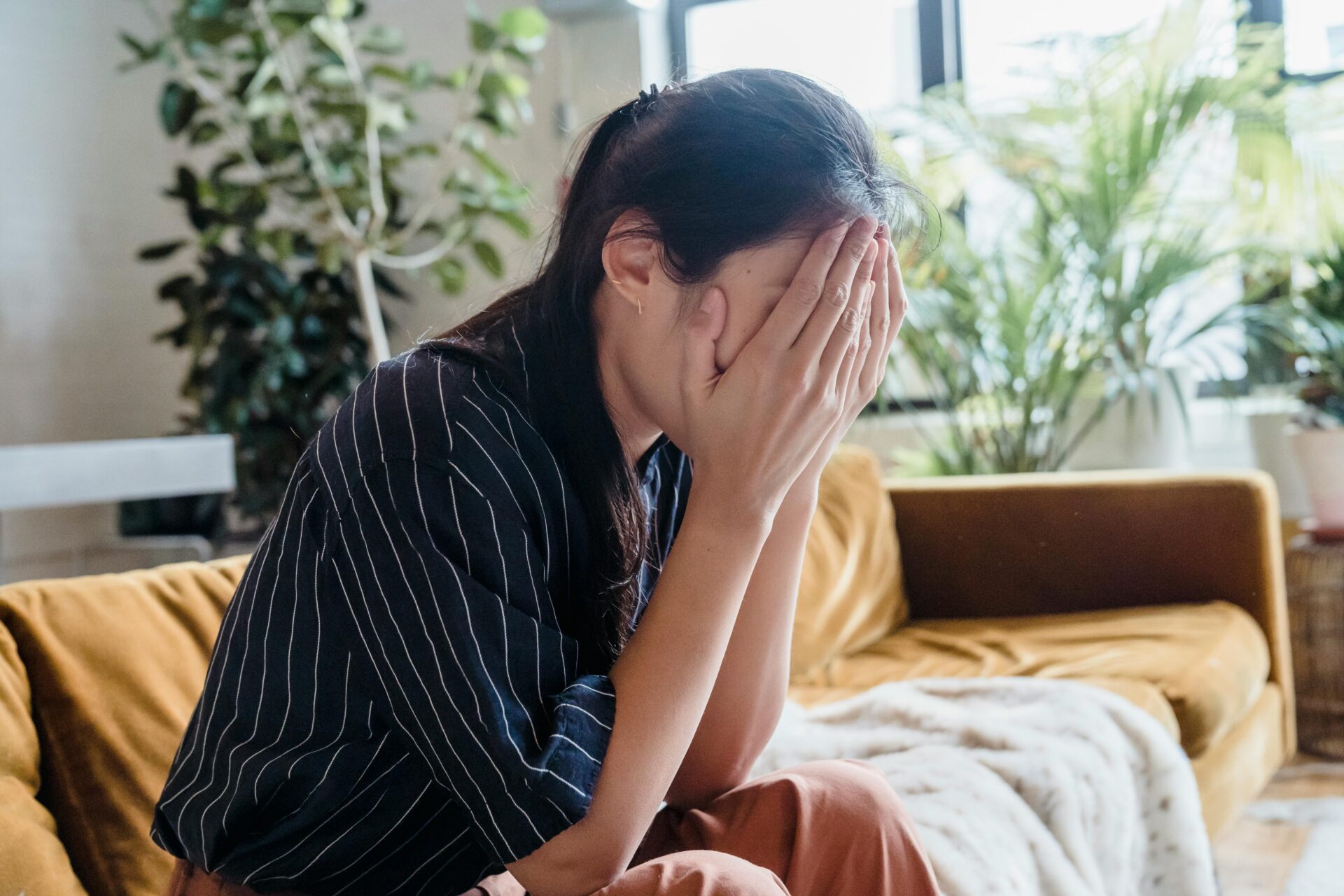 Women sitting on a couch putting her hands over her face in stress