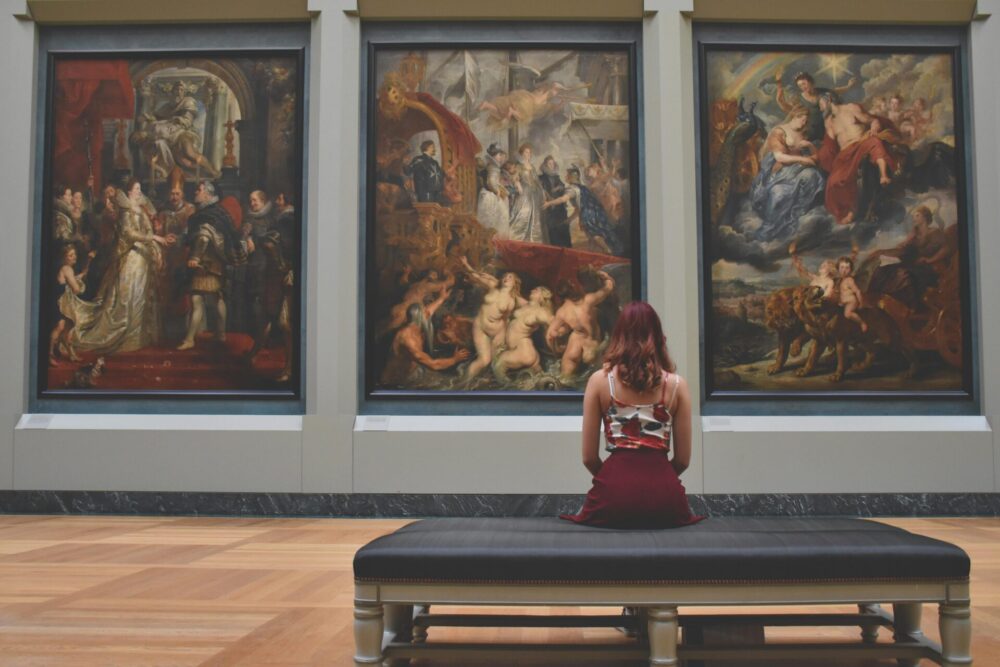 Woman sitting on ottoman in front of three paintings