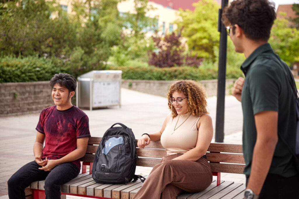 two people sitting on a bench and one person standing