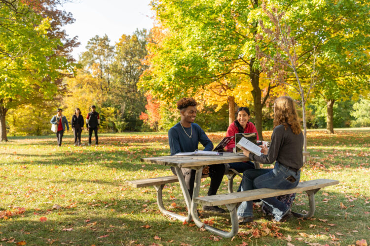 Students sitting on a picnic bench smiling and talking to each other