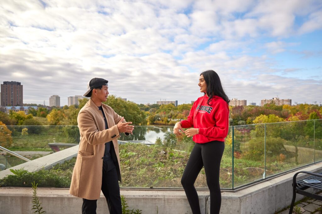 Two students talking on a terrace overlooking trees and pond