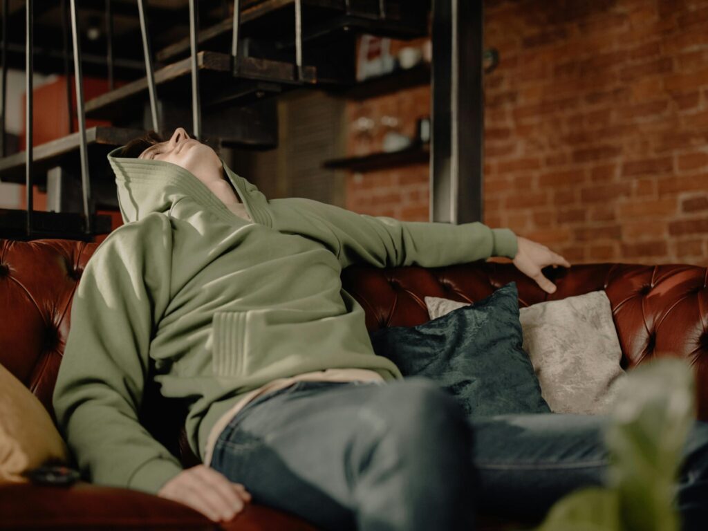 Man in hoodie sitting on brown leather couch and looking up