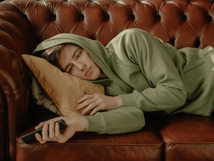 Main in hoodie lying on brown leather couch