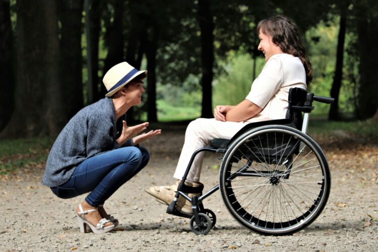 Person sitting in wheelchair and another person crouching in front of them