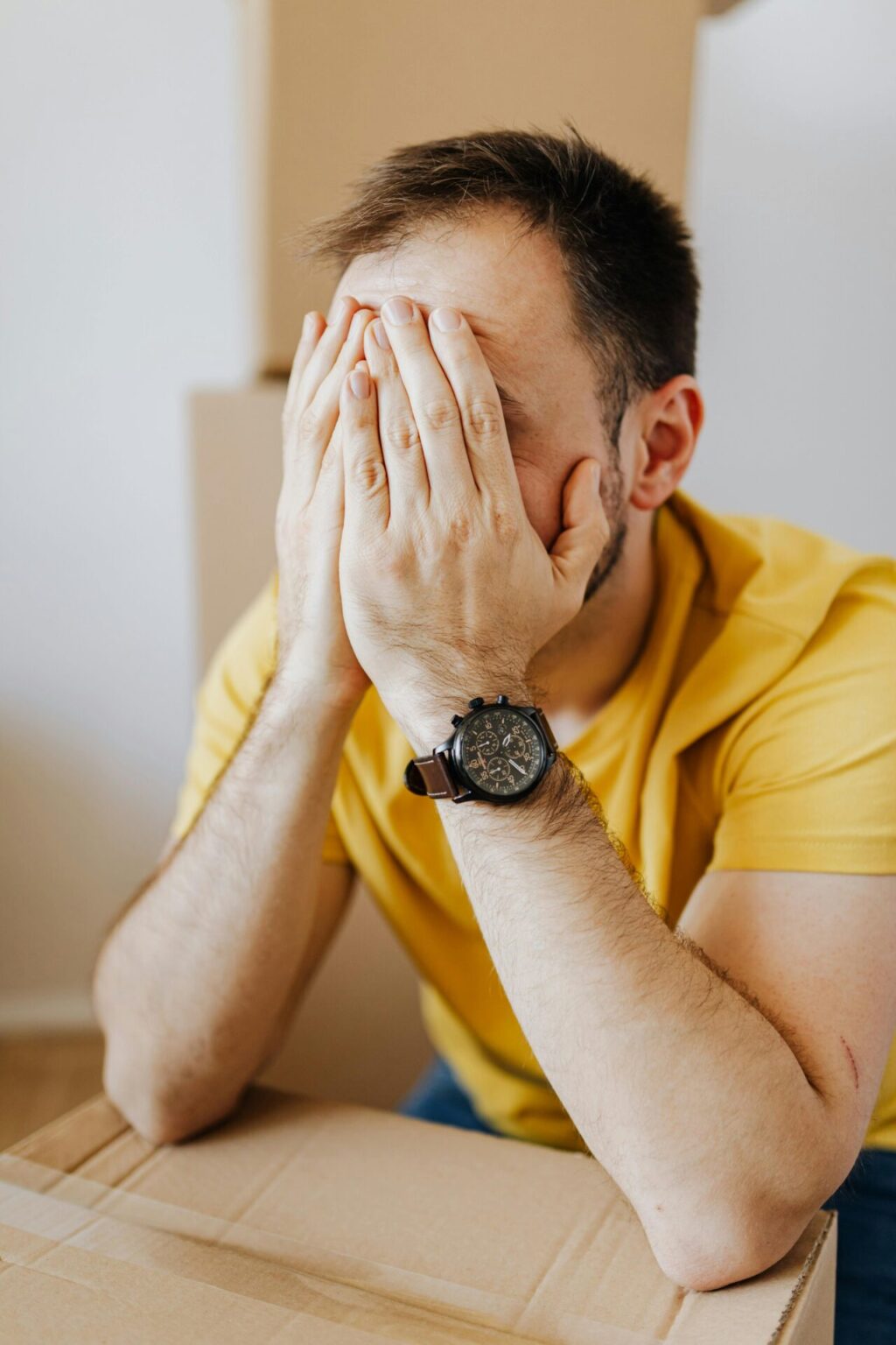 Stressed man covering face and leaning on carton box