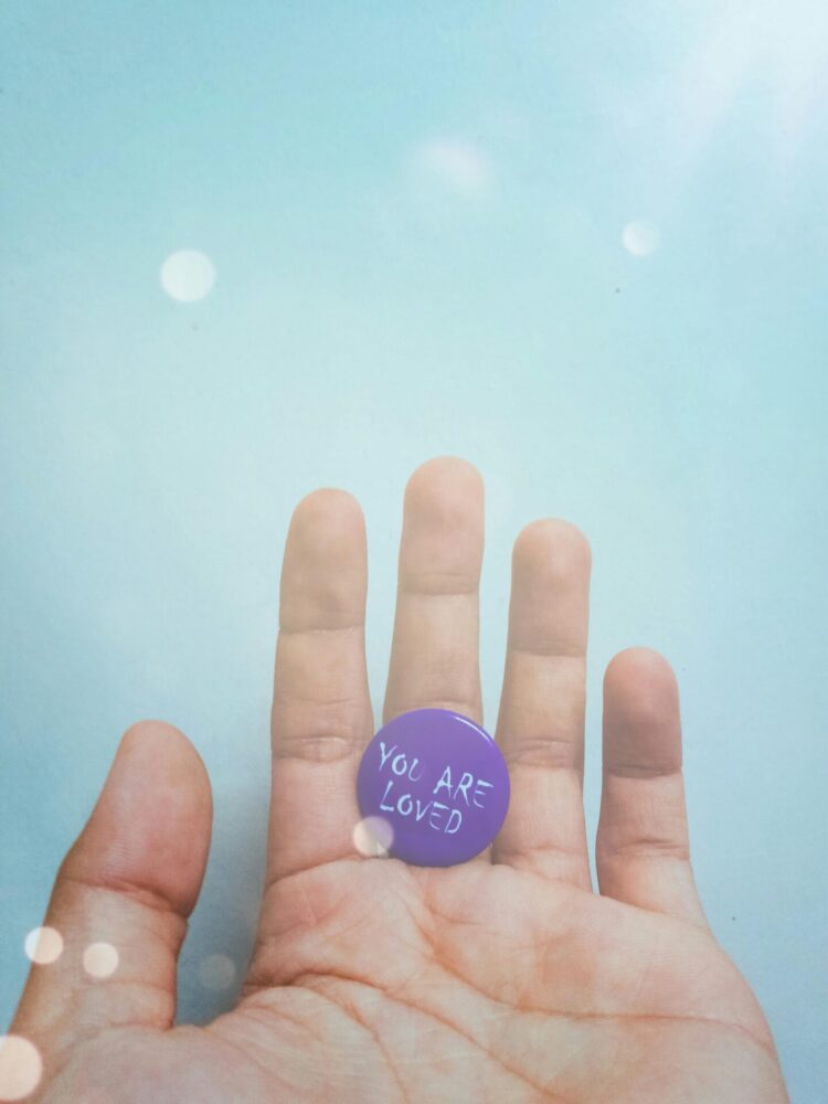 Person hold purpose badge with "you are loved" text