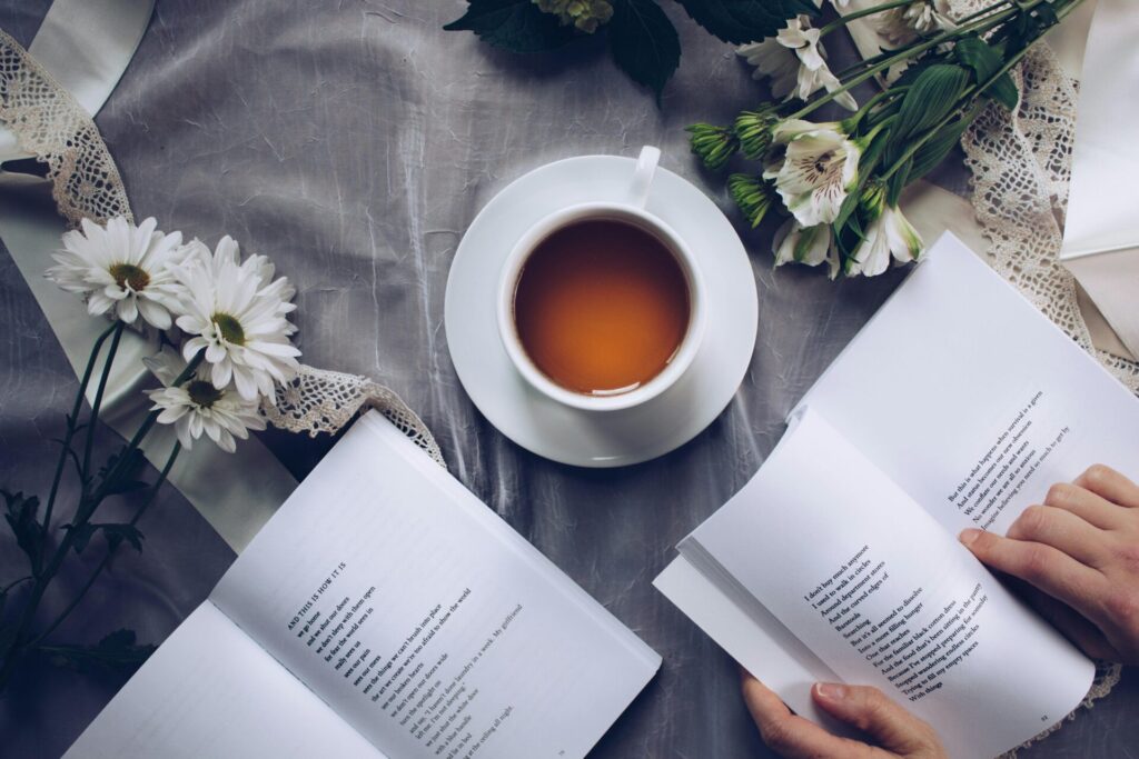 White ceramic teacup with saucer near two books and flowers