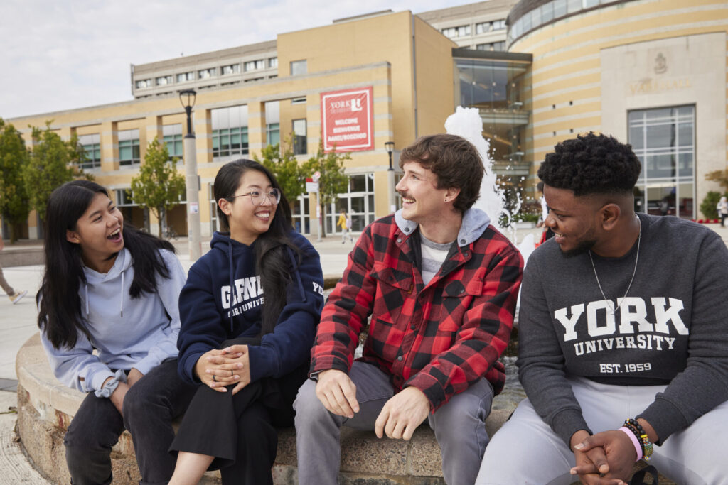 Four friends sitting in front of a fountain and smiling