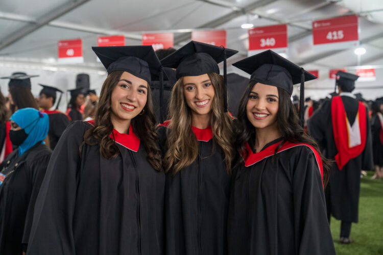Three students at a convocation ceremony looking and smiling at the camera