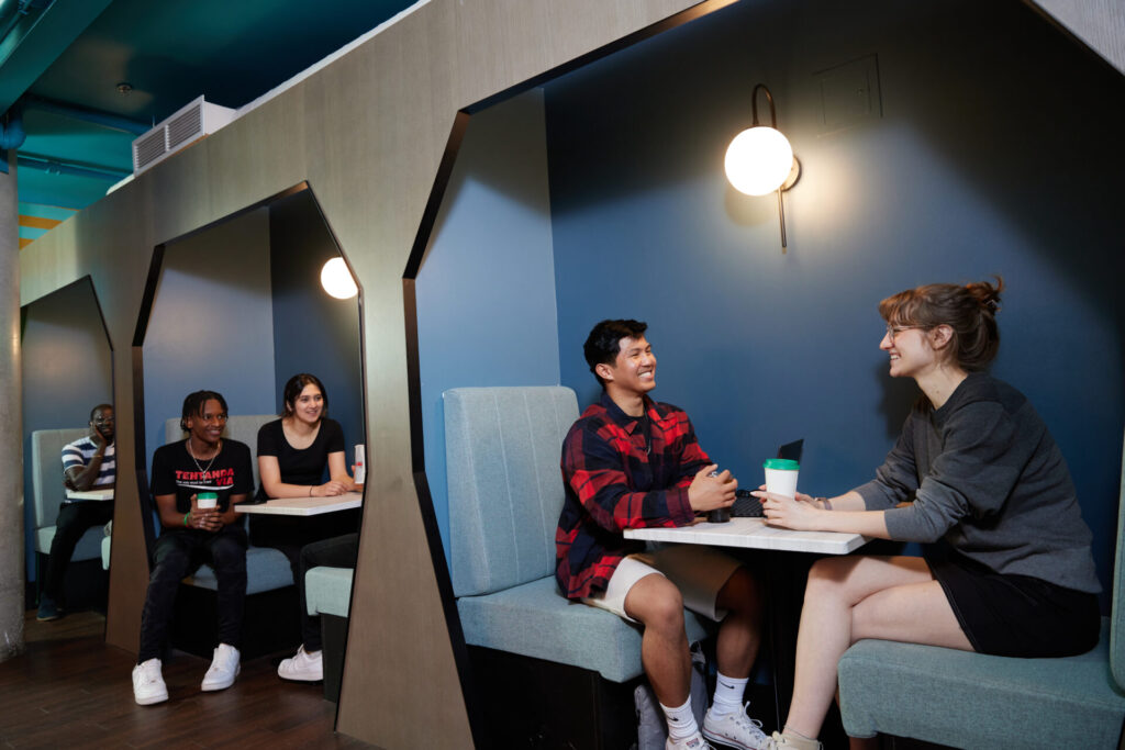 York University students sit in cozy booth-style seating areas, chatting and enjoying coffee together in a lounge