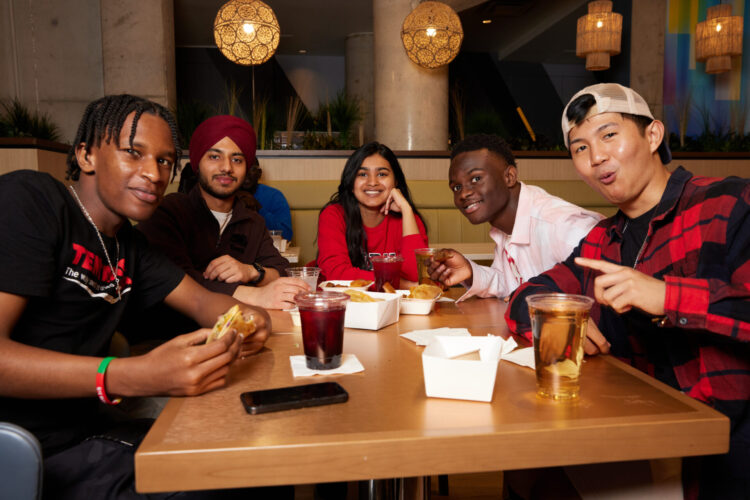 York University students sit together around a table sharing food and drinks