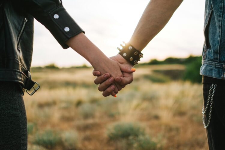 Couple holding hands while walking through a grassy field, symbolizing love, connection, and togetherness in a natural outdoor setting.