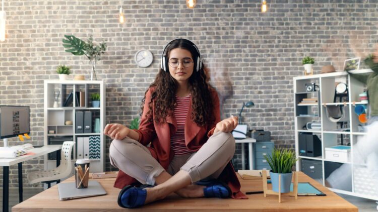 Woman meditating on the floor beside a laptop in a calm indoor space.
