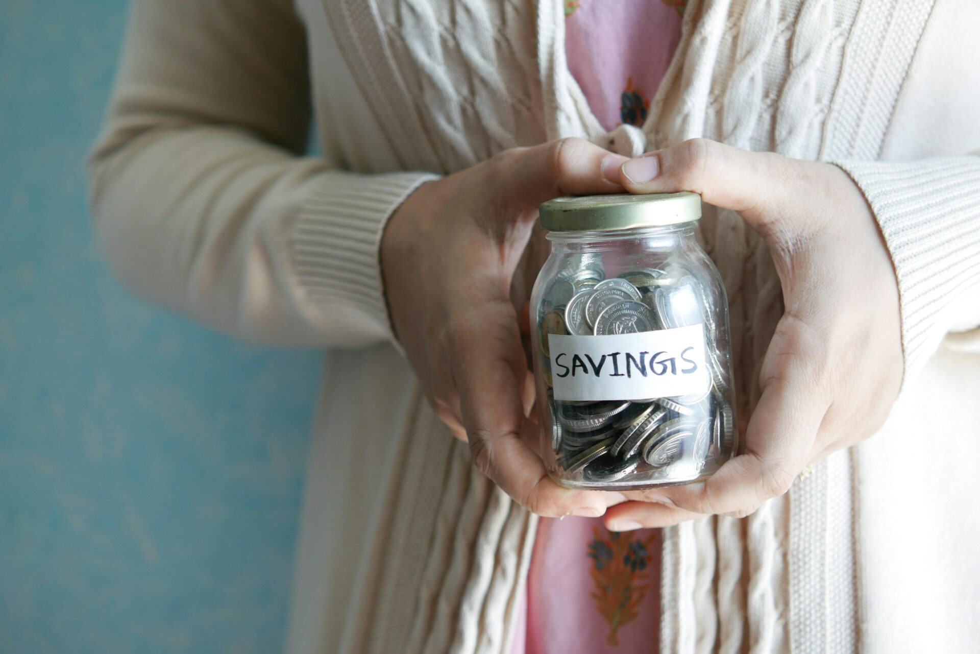 Person holding a glass jar filled with coins labeled “savings